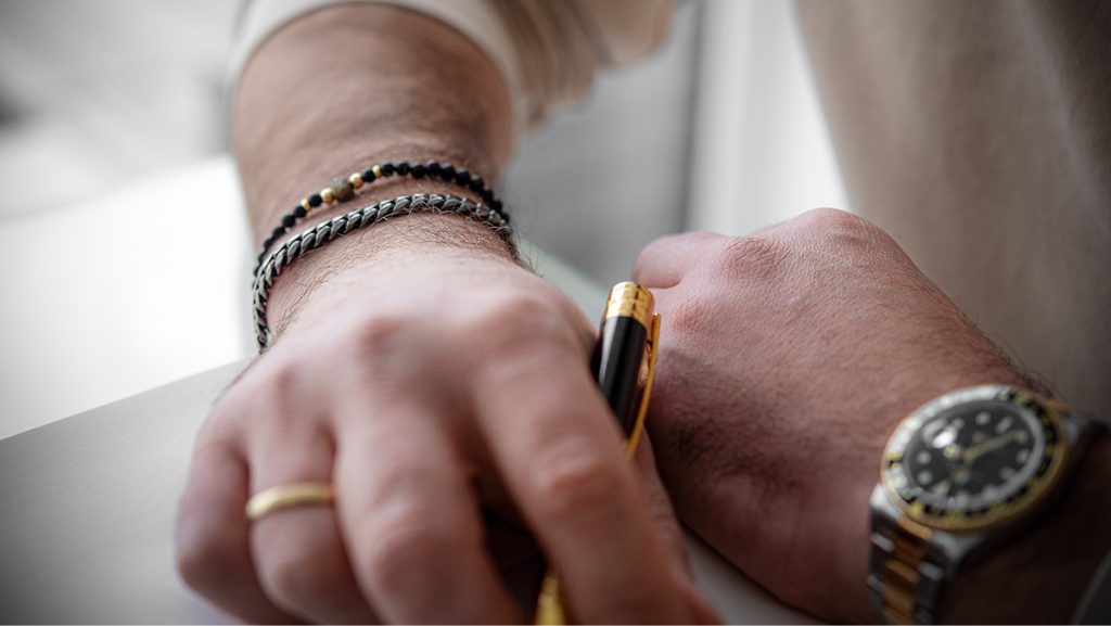 Mann trägt schlichte Armbänder, Goldring und Rolex-Uhr