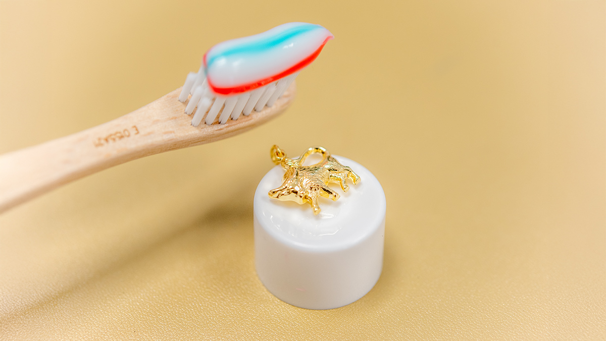 Goldener Anhänger, daneben Zahnbürste mit Zahnpasta zur Reinigung