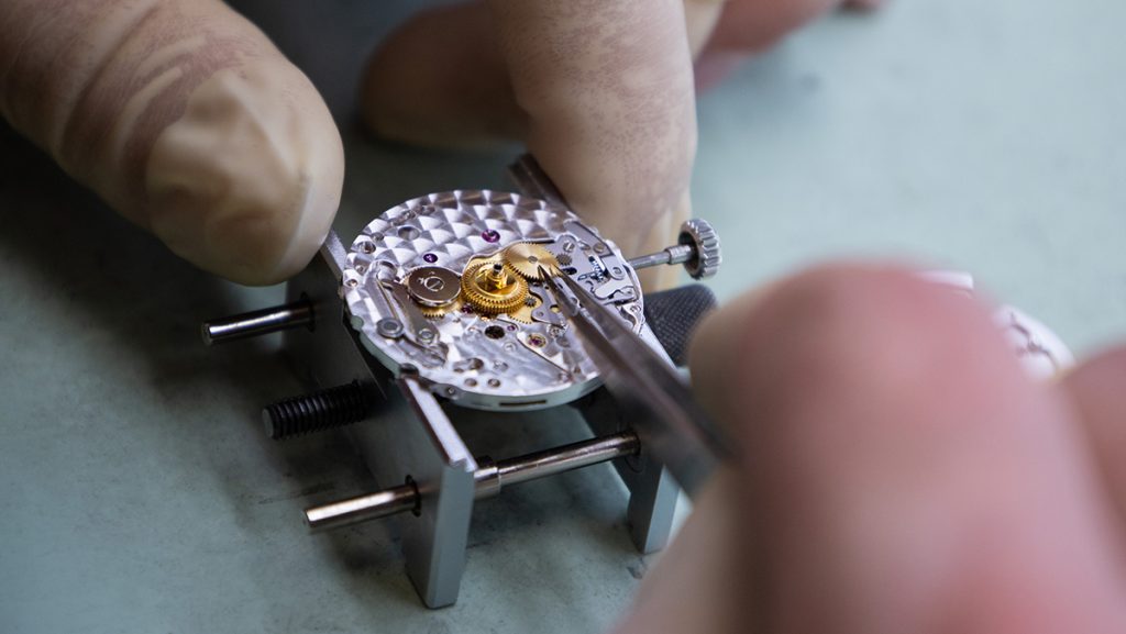 Uhrmacher setzt Einzelteile im Uhrengehäuse ein